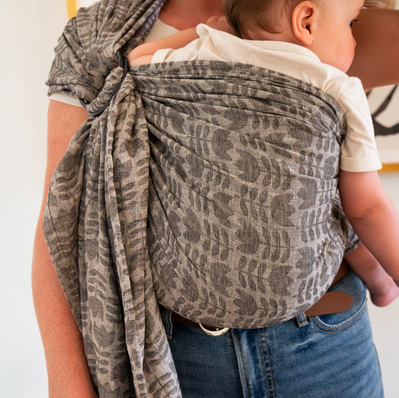 Woman holding a baby in a gray woven floral ring sling