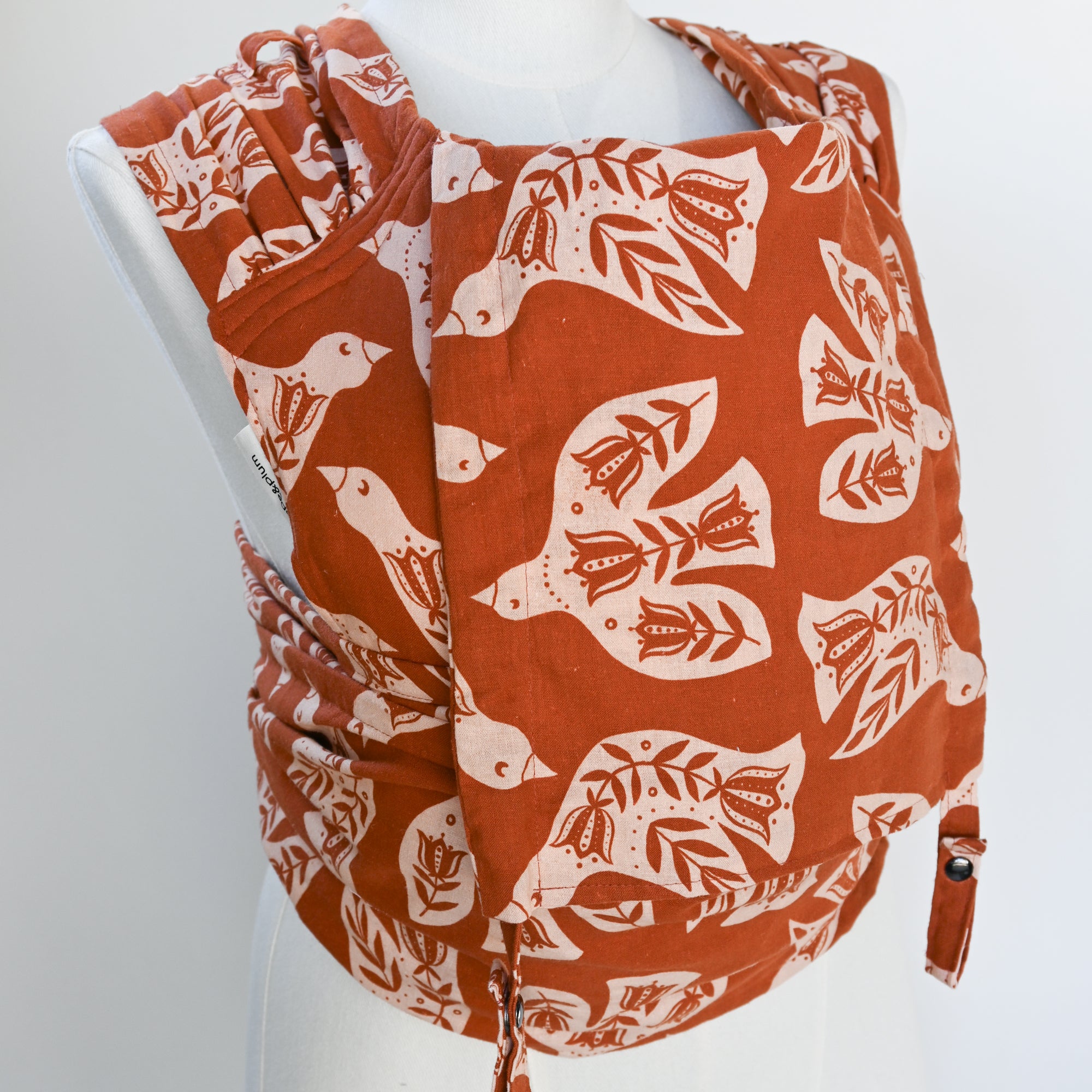 Meh Dai Baby Carrier in Wren — clay ground with white folk-art illustrated birds and floral tail motifs