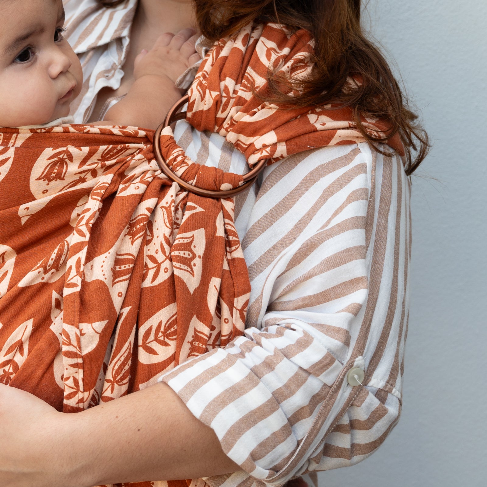 Ring Sling in Wren — clay-toned fabric with cream folk-art bird and floral illustrations, copper rings.