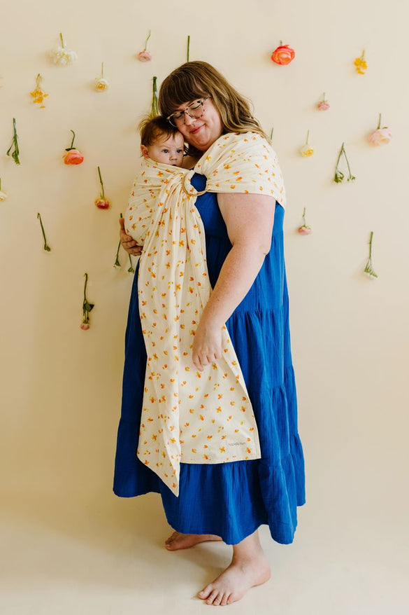 Plus-size mother wearing infant in plus-size sunflower print ring sling