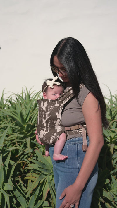 Sprout Newborn Carrier in Rodeo — caregiver in glasses kissing a newborn's head, mustang print carrier, aloe plants behind.