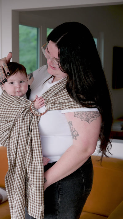 Ring Sling in Clove — caregiver holding a baby in the gingham sling, at home.
