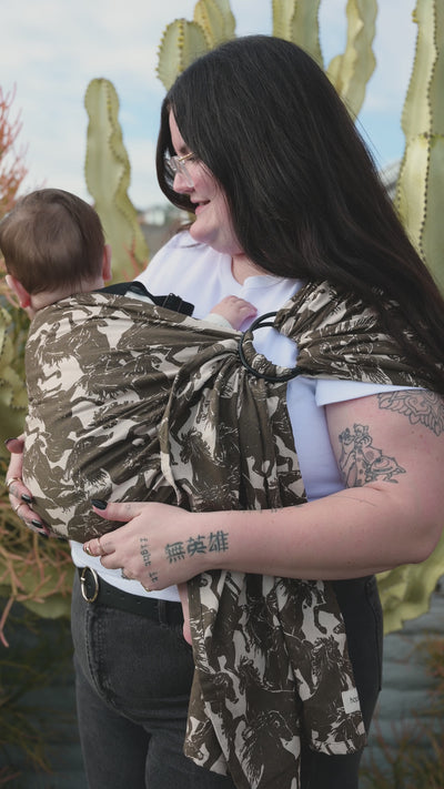 Ring Sling in Rodeo — back view of a caregiver carrying an infant in the draped mustang print sling, cactus garden behind.