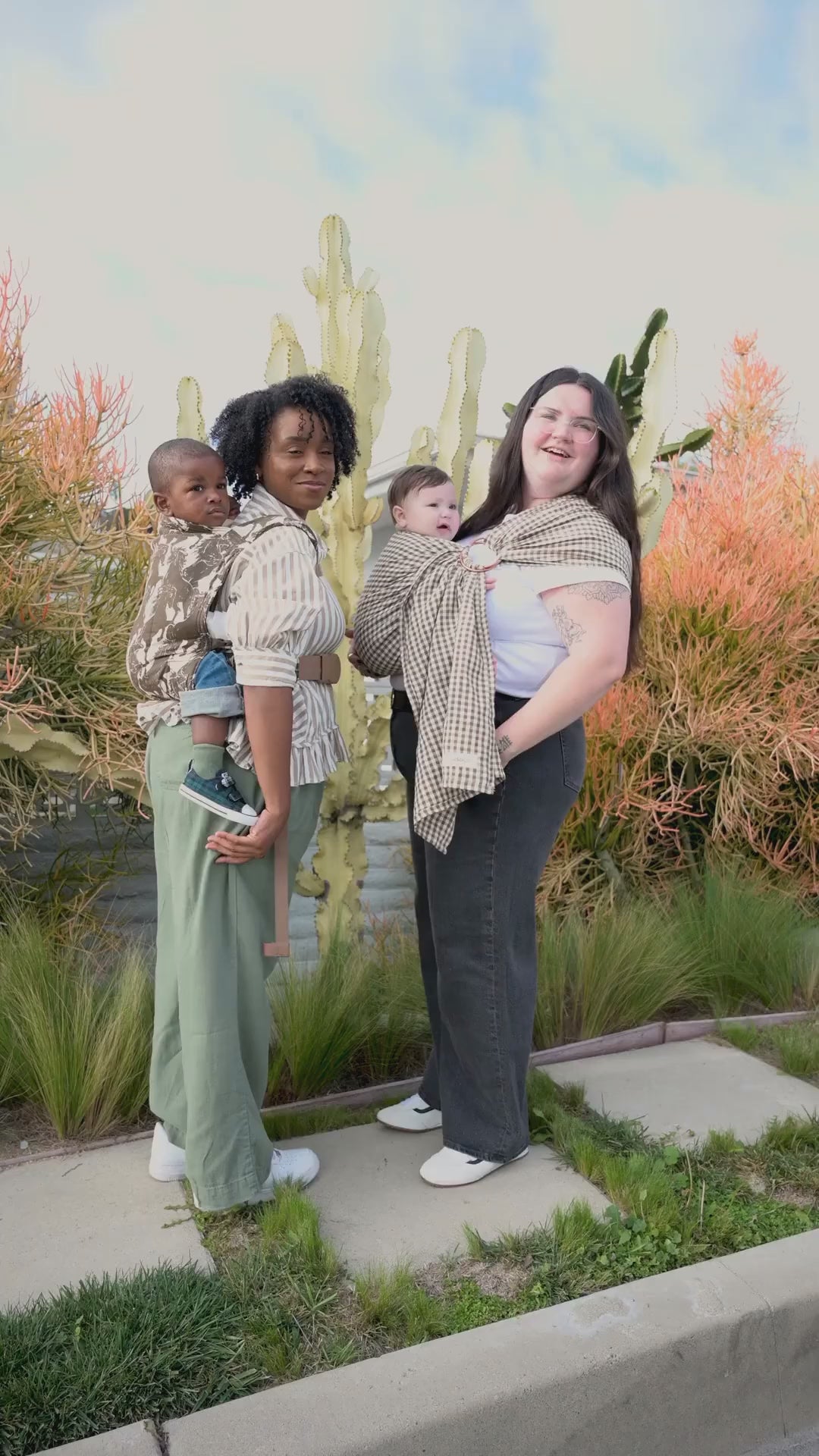 Editorial video for the Rodeo and Clove baby carrier collection, showing both carriers worn outdoors and indoors: two women carrying a toddler and baby in the horse-print Rodeo carrier and gingham Clove ring sling by a cactus garden, plus close-ups of a woman in a cowboy hat and a father wearing the carriers with their children.
