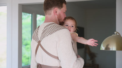 Lark Baby Carrier in Clove — caregiver smiling down at a toddler hugging him in the gingham carrier, at home.