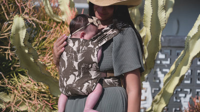 Sprout Newborn Carrier in Rodeo — caregiver in a straw hat holding a newborn close in the mustang print carrier, cactus behind.