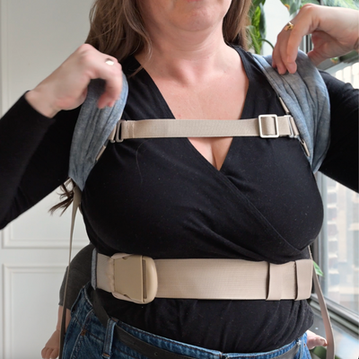 Video demonstrating how to adjust the chest clip on the Lark baby carrier: the wearer points to the buckle, then slides it upward along the shoulder strap to reposition it for a better fit.
