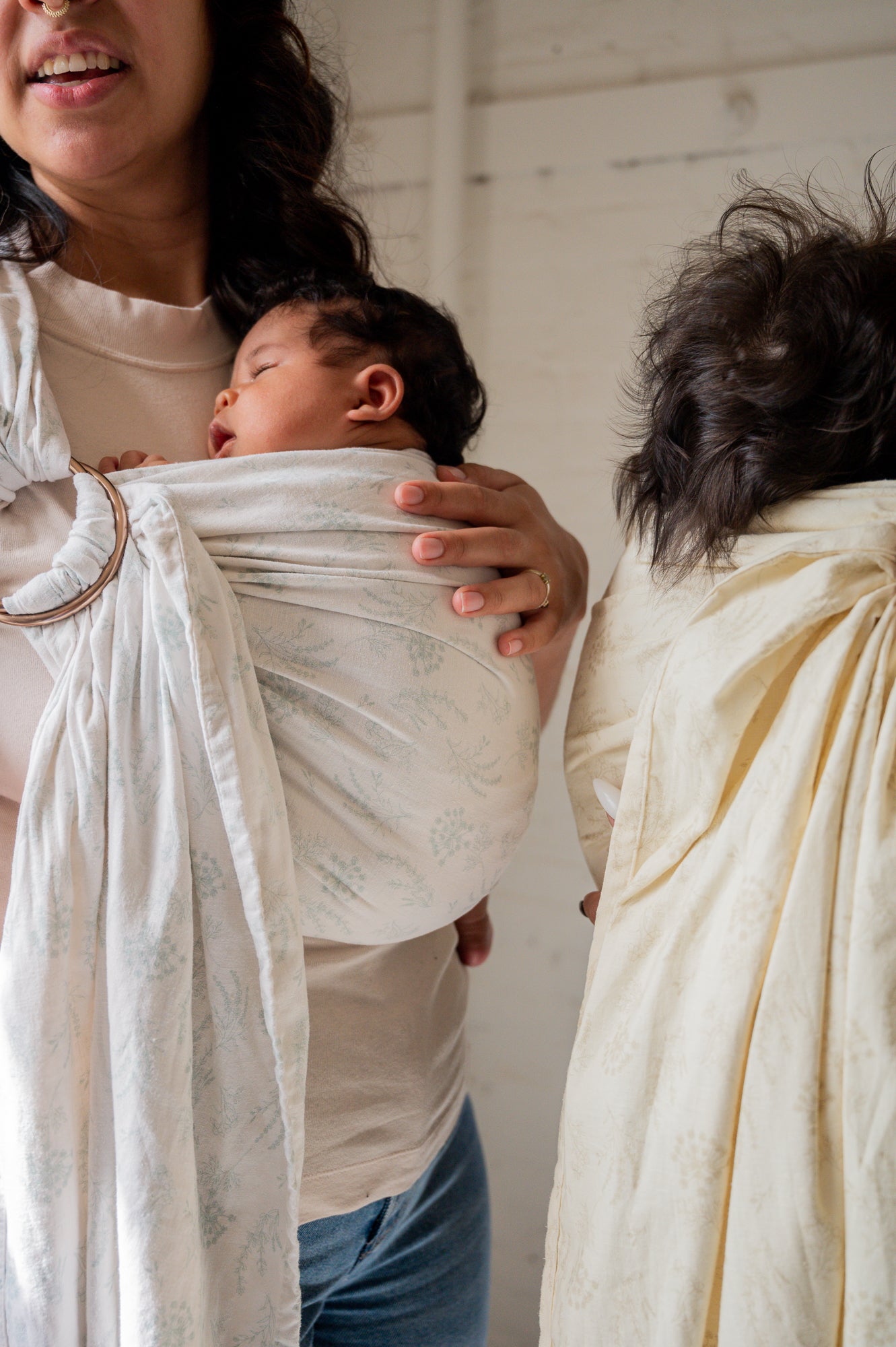 Two mothers holding their infants in ring sling baby carriers