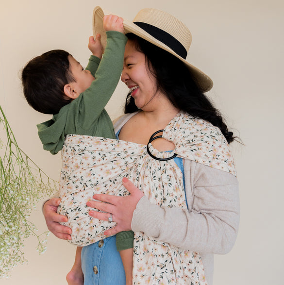 Mother holding son in floral print ring sling carrier smiling. 
