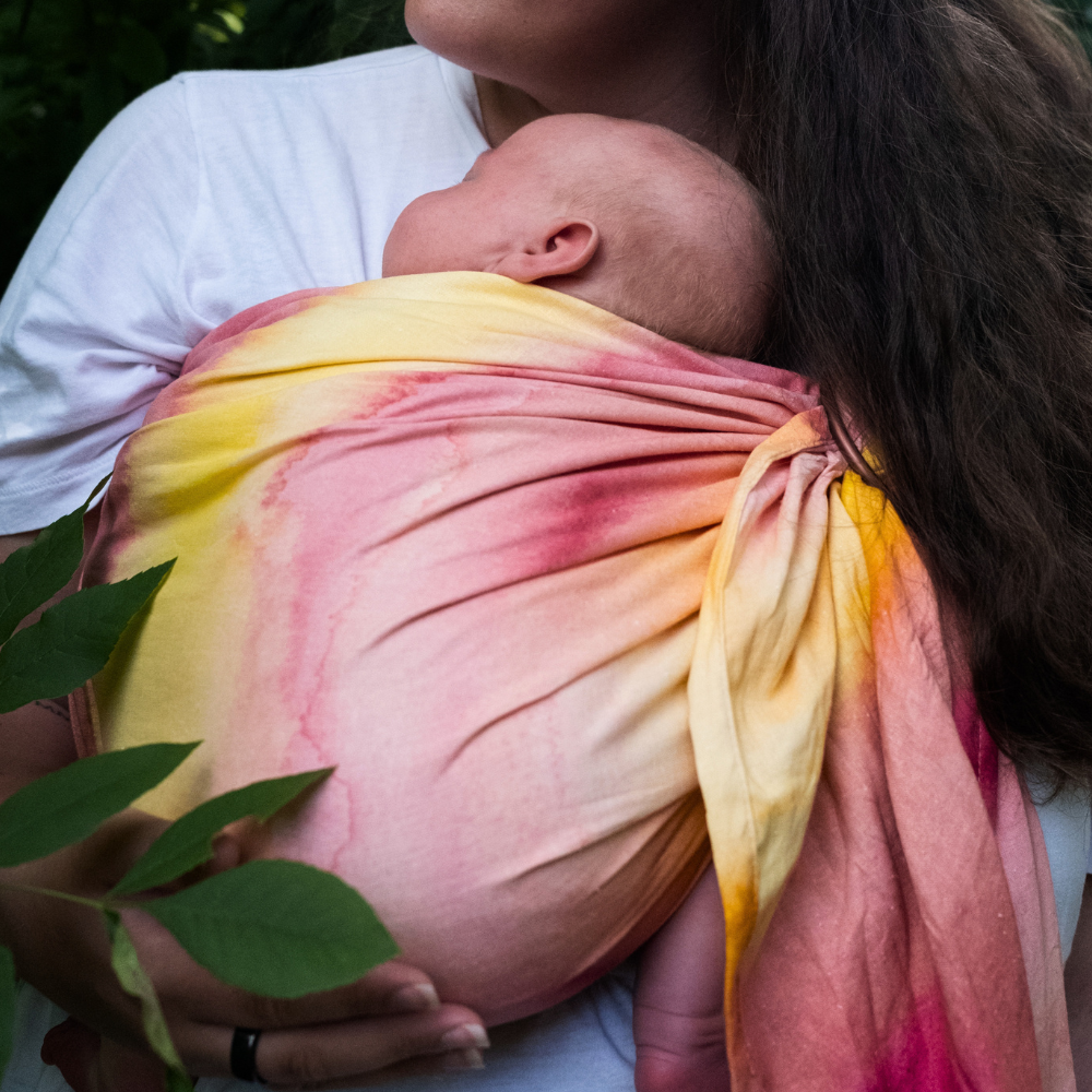 small infant being carried in a watercolor sling with yellow and pink hues