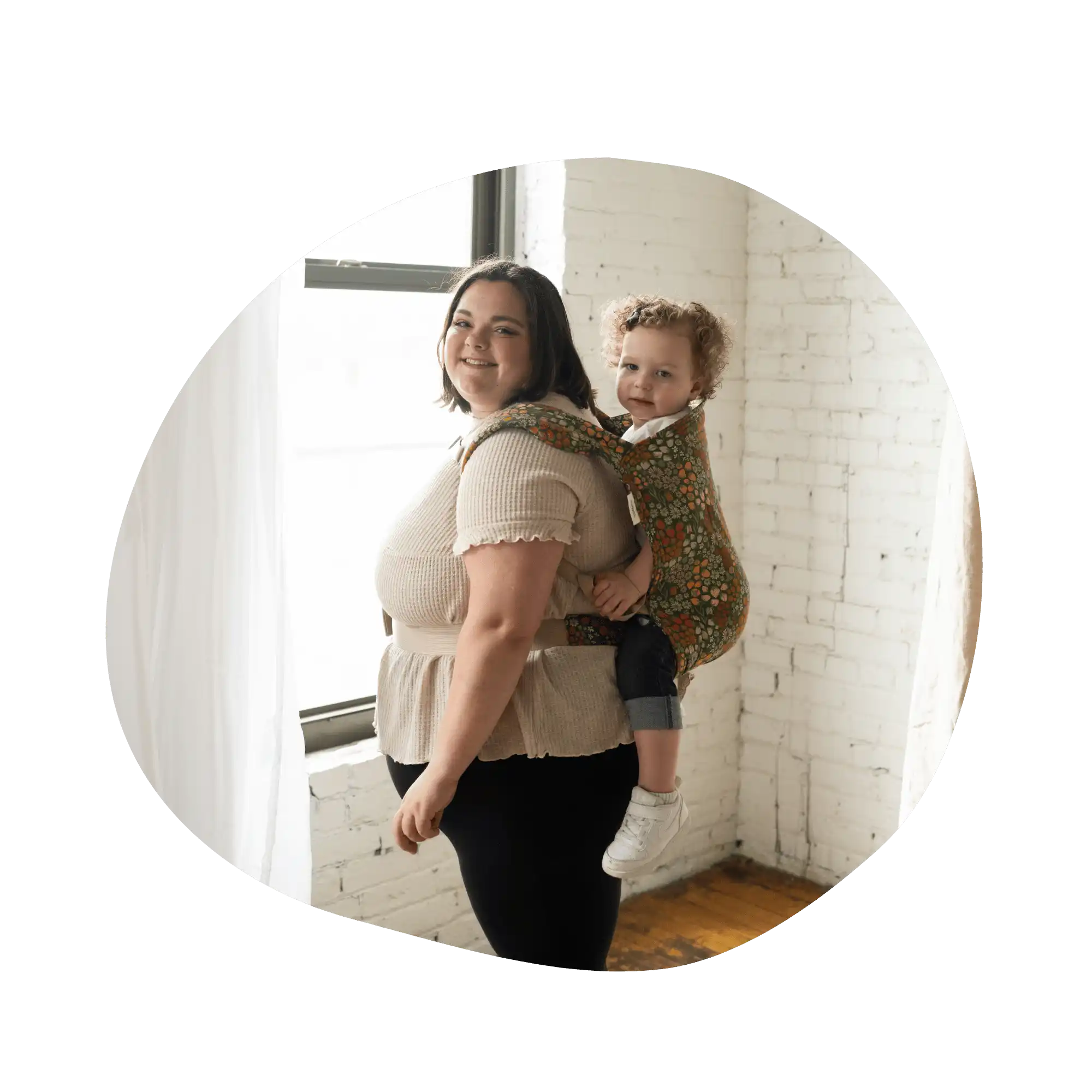 Woman carrying child in floral baby carrier.